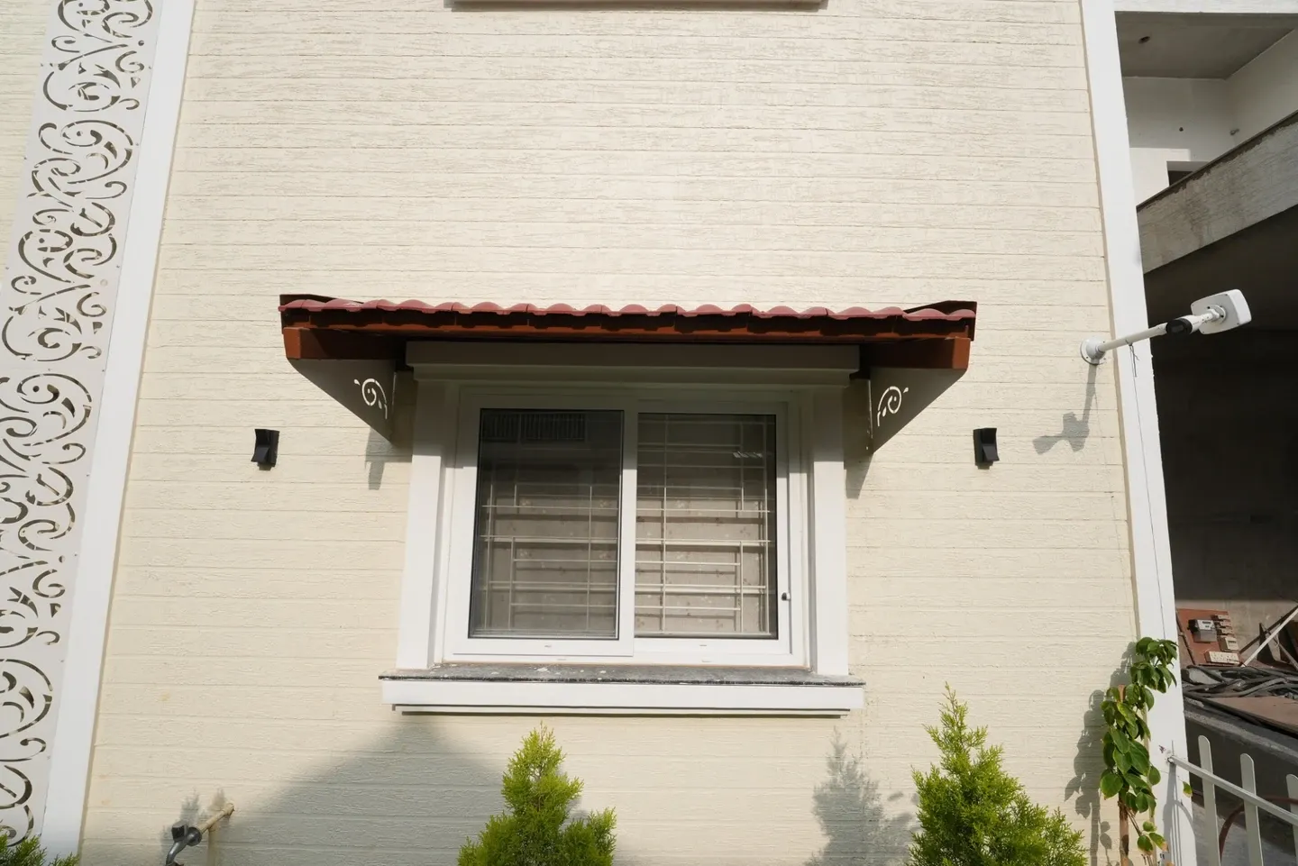 White-framed window beneath a red tile canopy on a pale brick wall