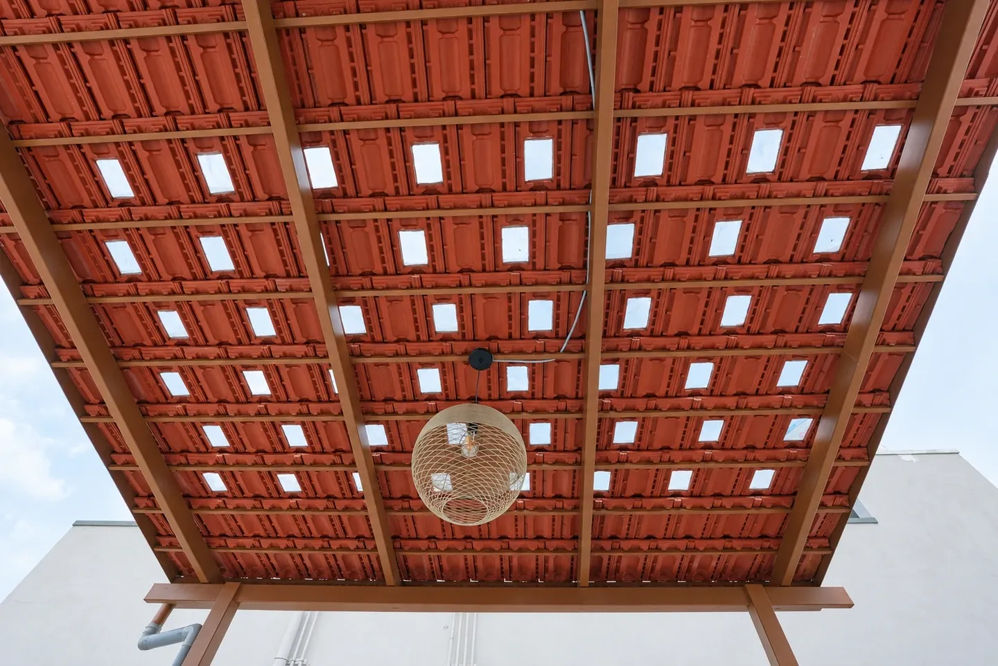 Underside of a red tiled pergola roof with glass daylight openings and a ceiling fan