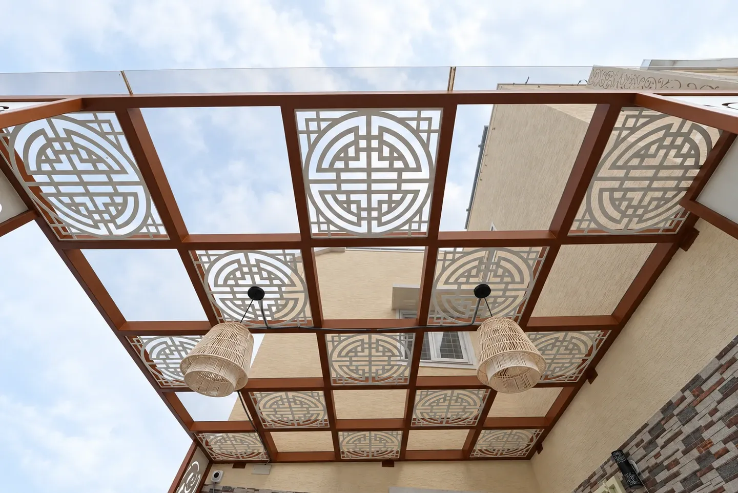 Upward view of geometric white panels and clear roof sections in a brown pergola frame
