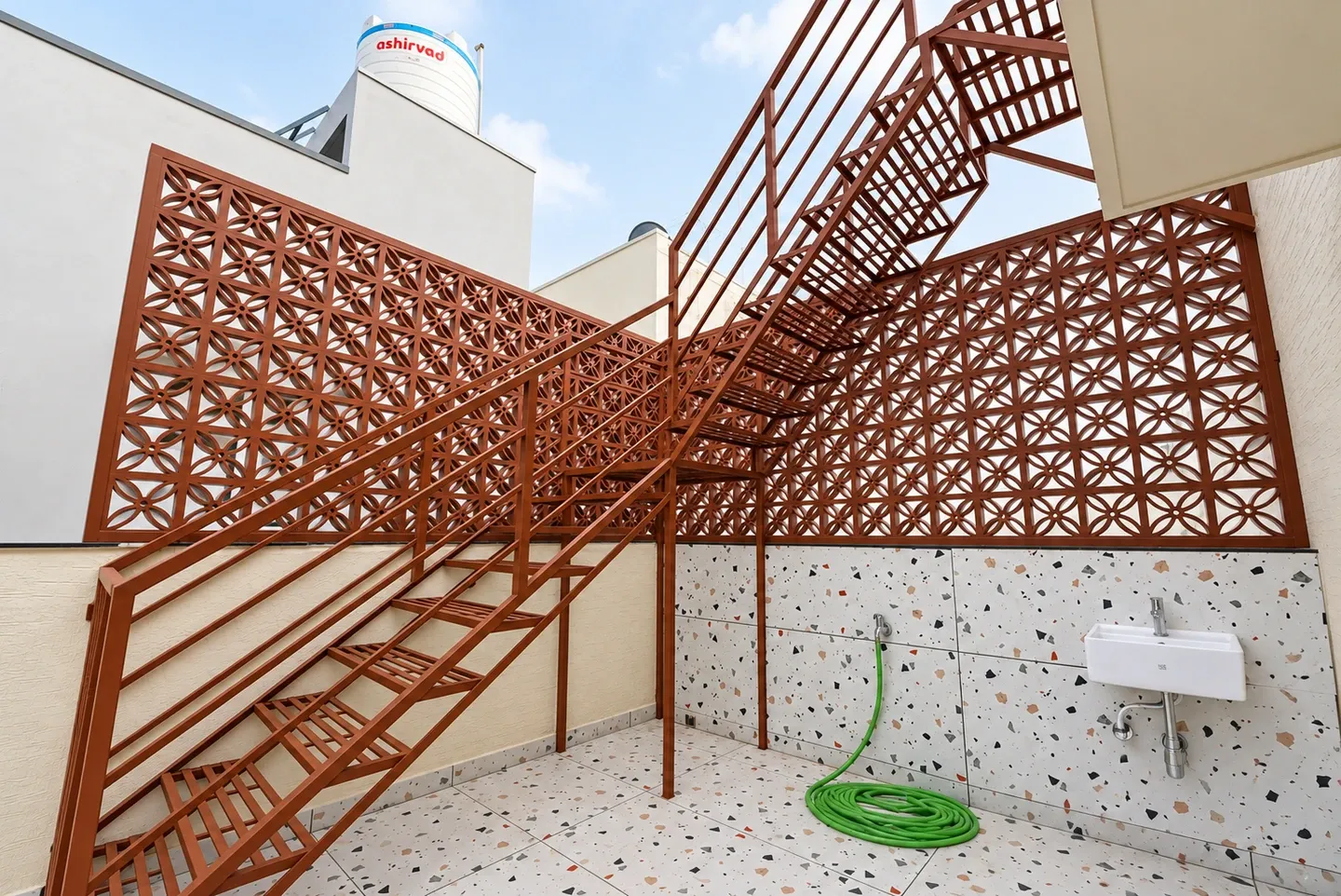 Brown metal staircase and railings beside a geometric jali screen