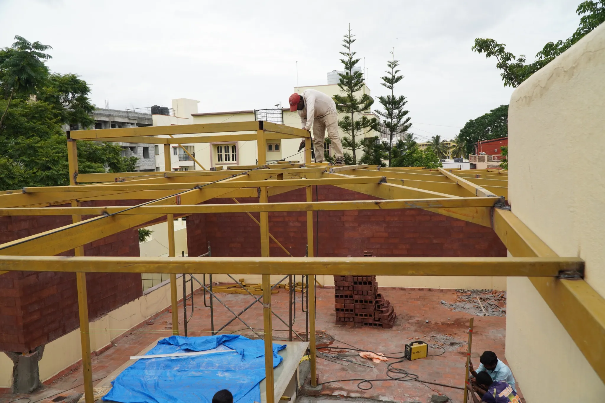 Fabricators assembling a steel roof framework between courtyard walls