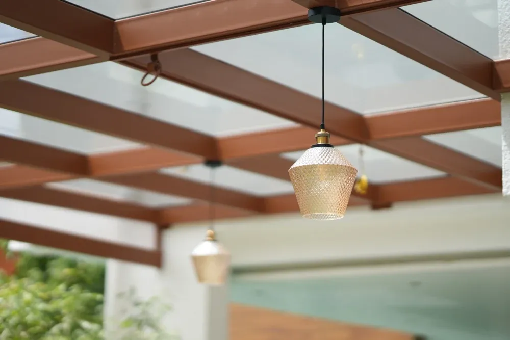 Pendant lights sit between the timber-toned beams of the glass pergola.