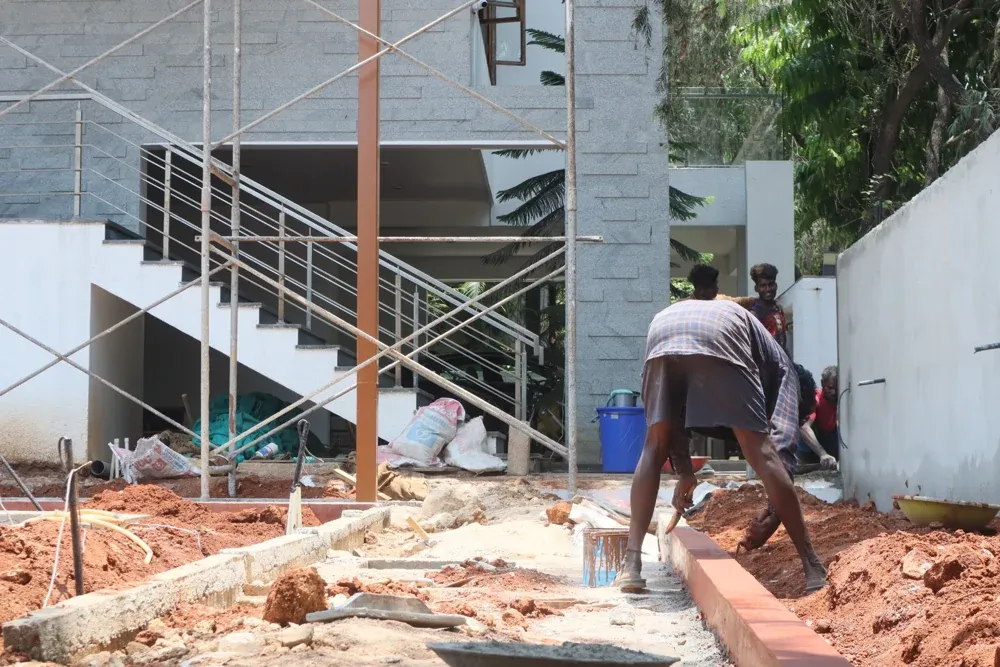 A worker prepares the outdoor ground beside the house and staircase.