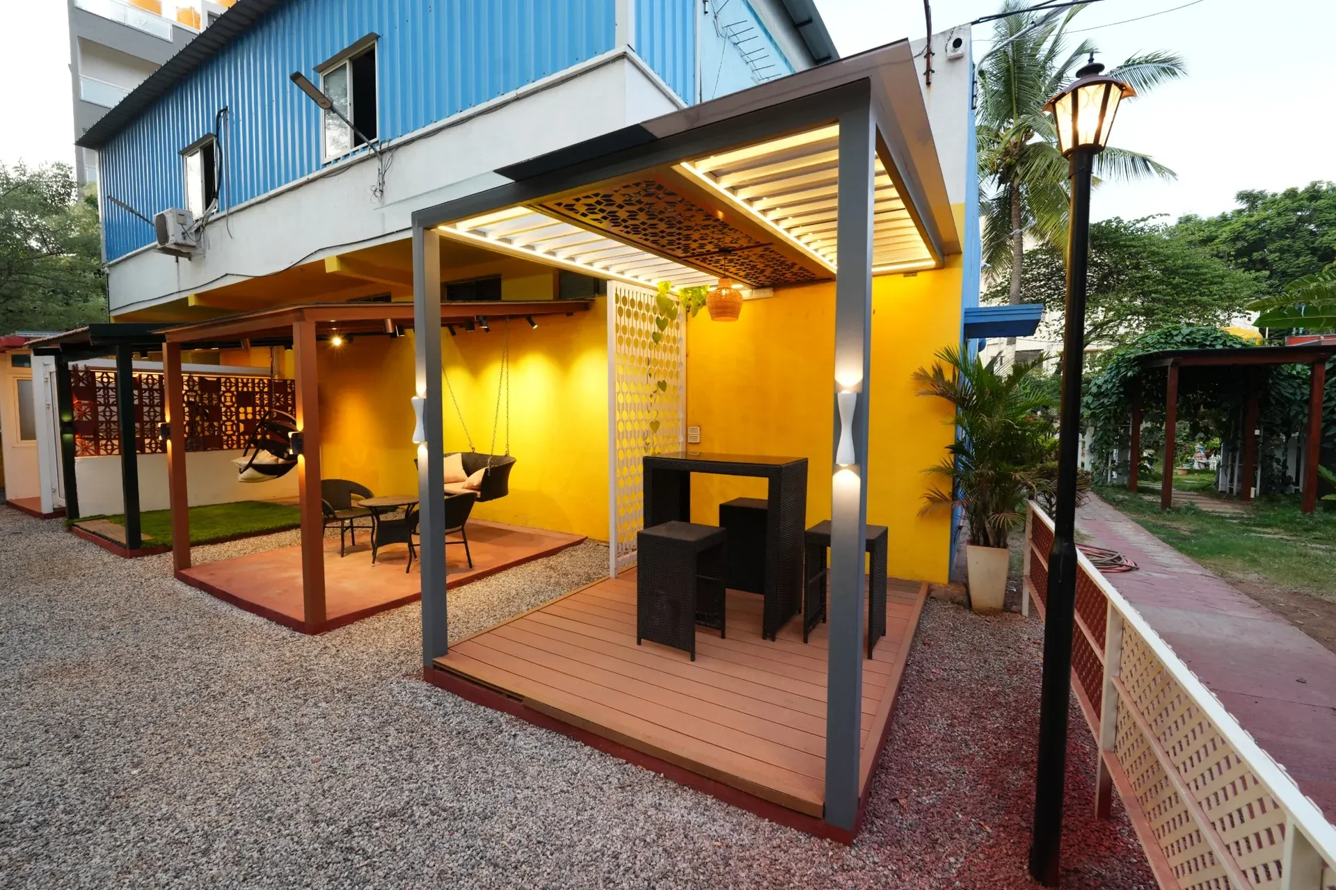 Wood-look deck and illuminated premium pergola display beside a yellow wall