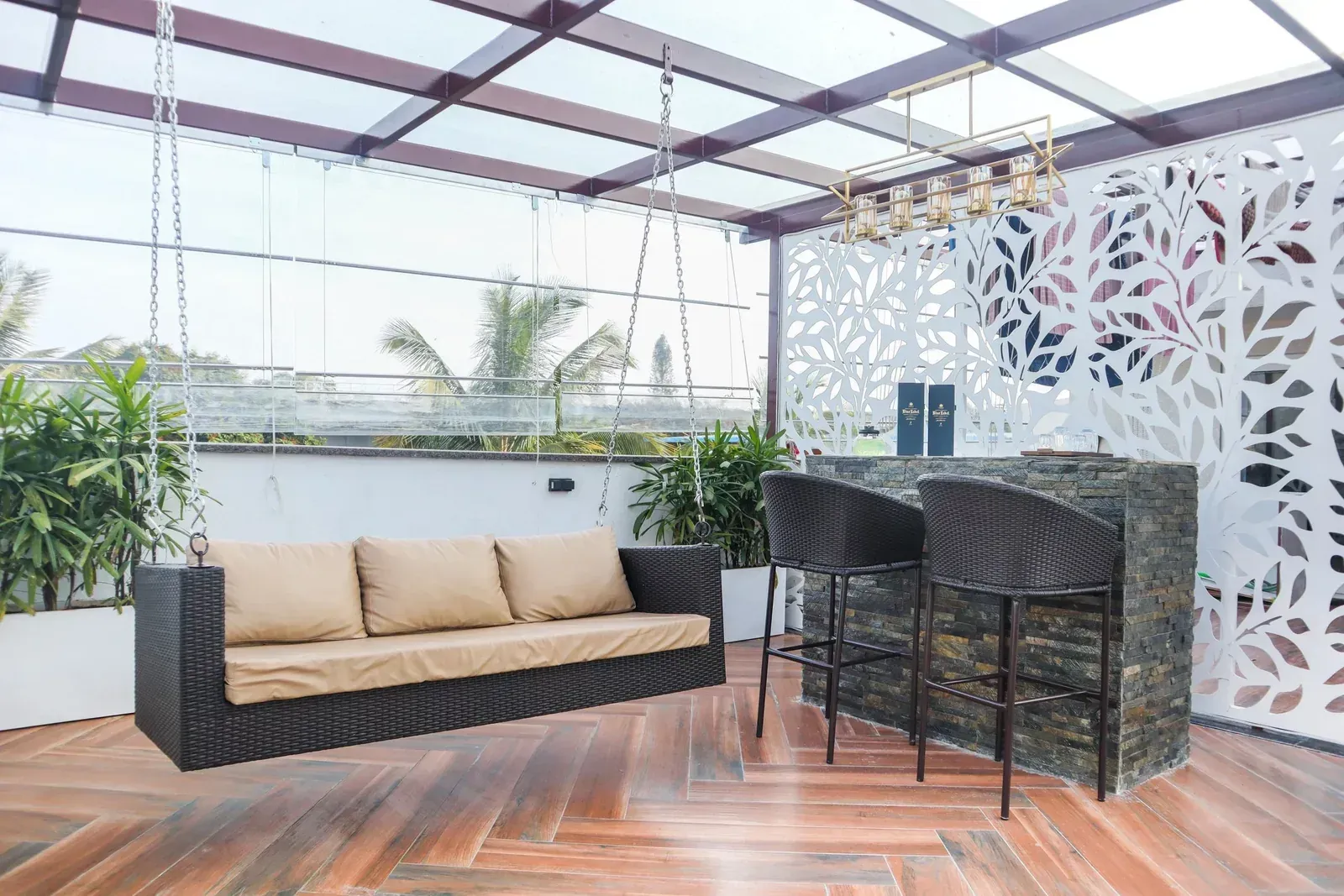 Glass-roof terrace with a suspended sofa, bar counter and white leaf-pattern privacy screen.