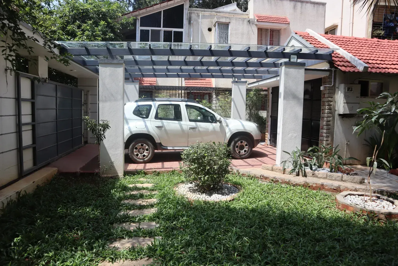Grey metal rafters and clear glass panels over a residential parking space with a white SUV.