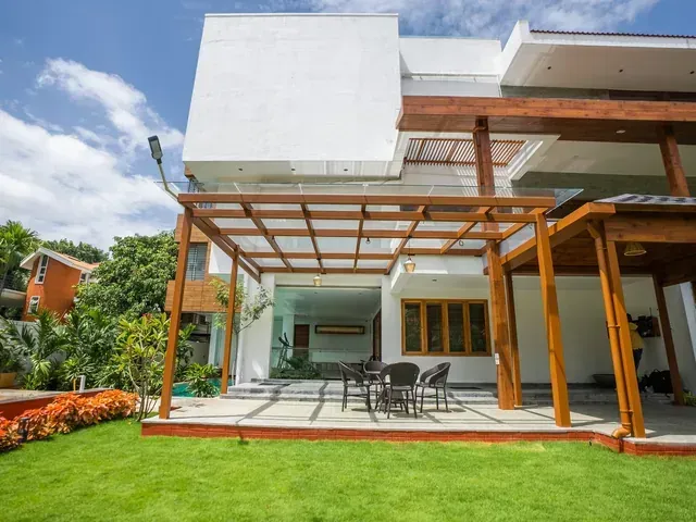 A brown metal and glass pergola sheltering a garden dining terrace