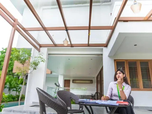 Outdoor dining beneath a glass roof supported by brown metal framing