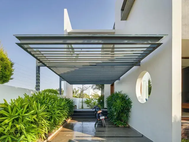 Slim glass canopy covering a narrow seating space beside a home