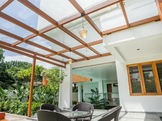 View from below of a brown pergola frame, clear glass roof and pendant lighting