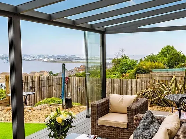 Garden lounge under a dark metal and glass pergola with an open city view
