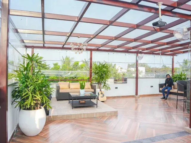 Wide view of a glass-covered terrace with sofa seating, a swing and a bar counter