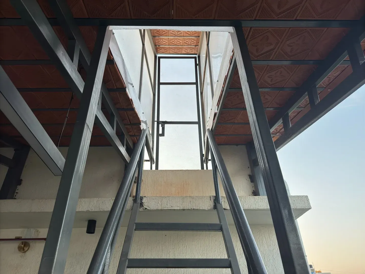 Upward view of a metal staircase and handrails beneath the terrace roof