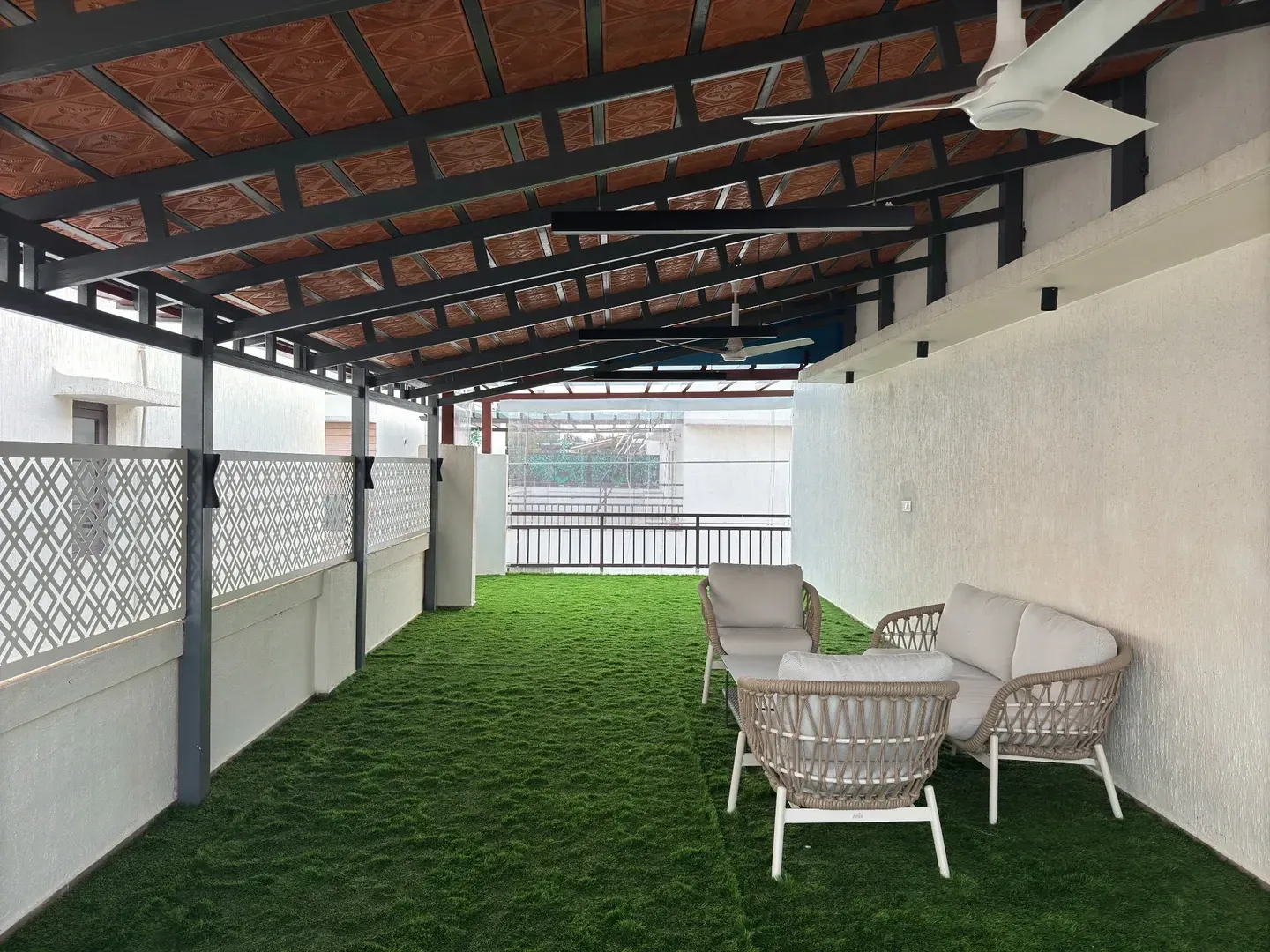 Long covered terrace with green flooring, pale outdoor chairs and a tiled roof