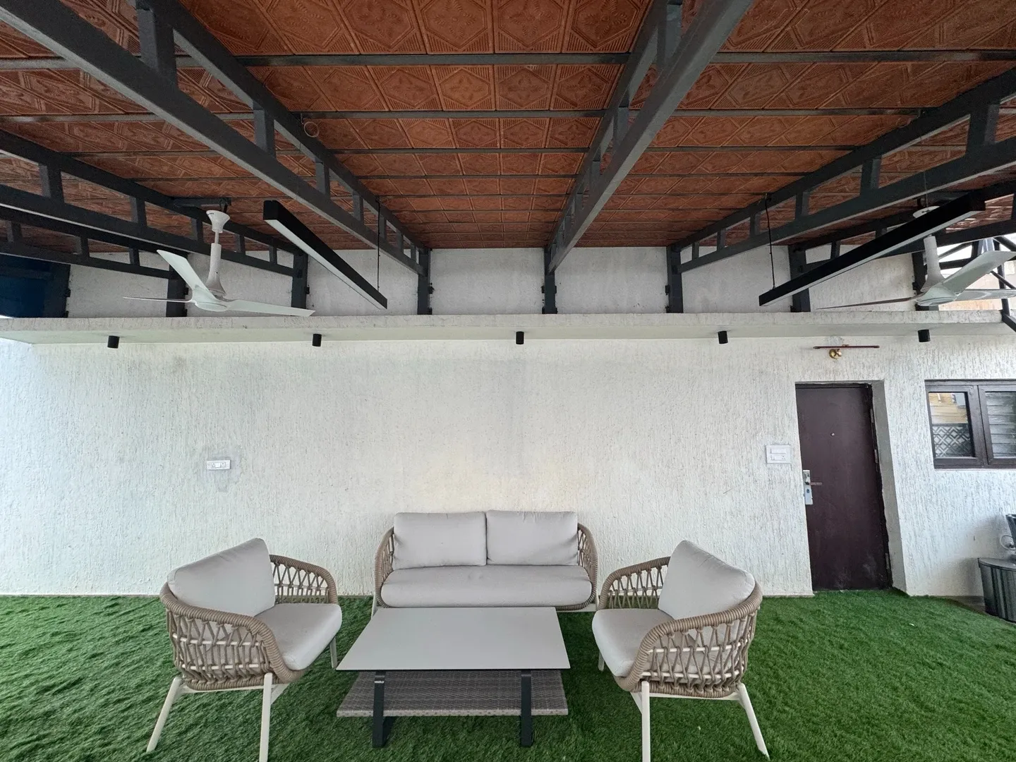 Outdoor sofa and chairs against a pale wall beneath a red tiled pergola