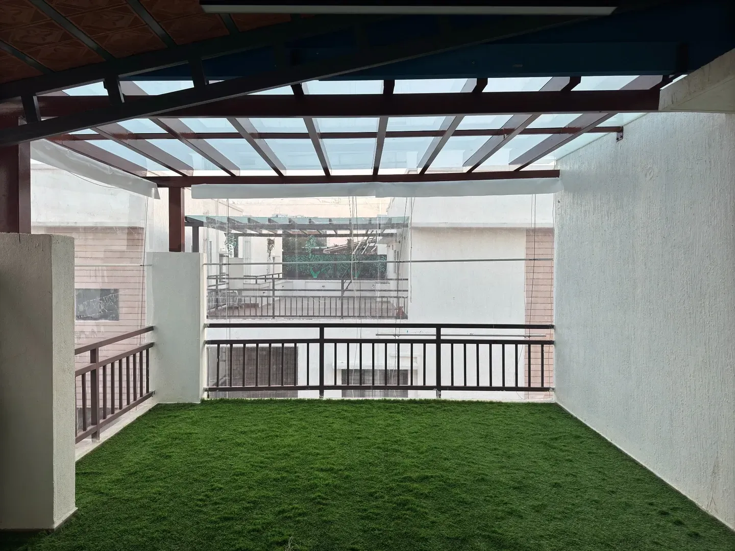 View from beneath the tile roof towards a glass pergola with dark framing