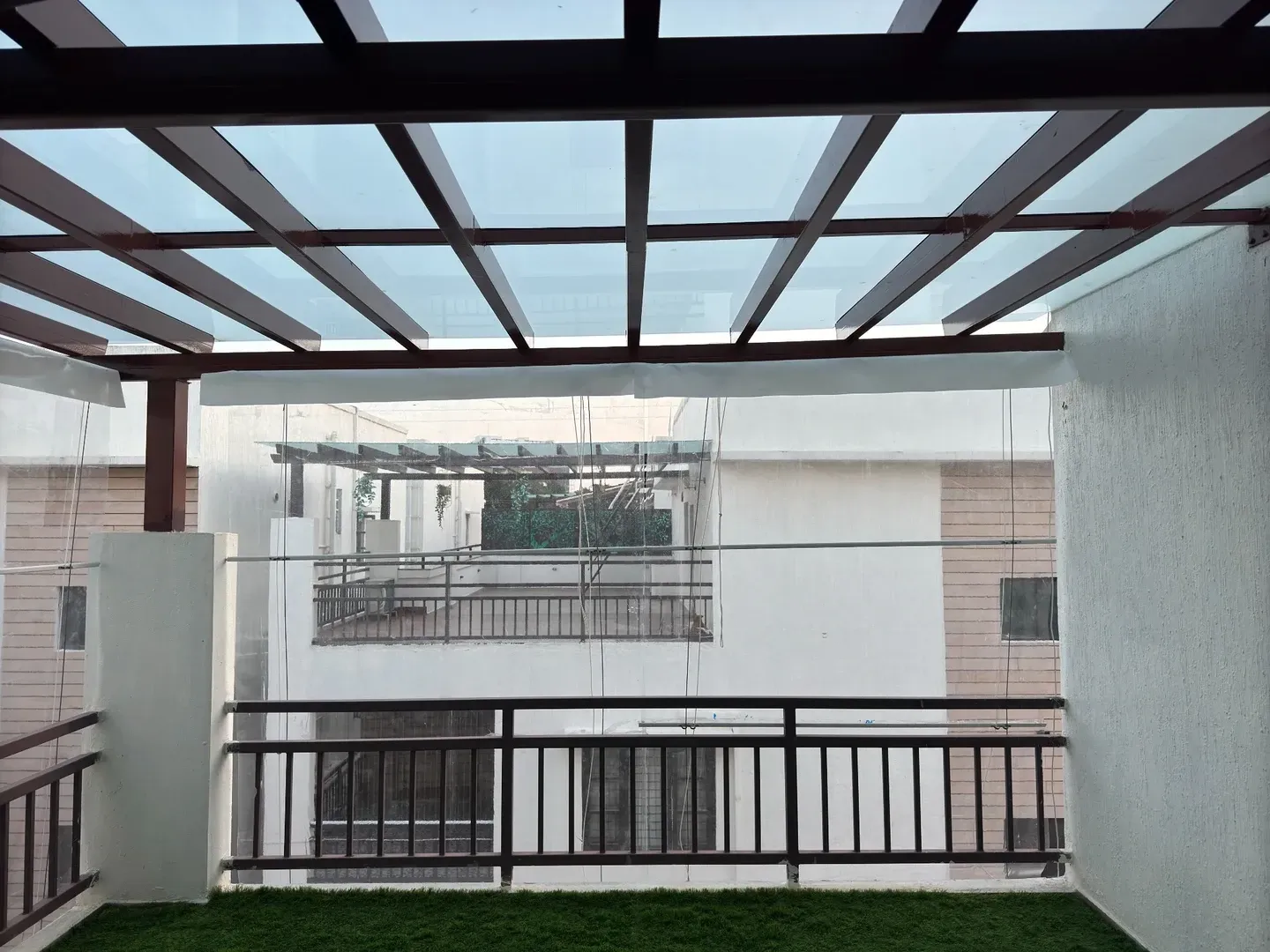 Glass pergola roof divided by dark metal rafters above a black railing
