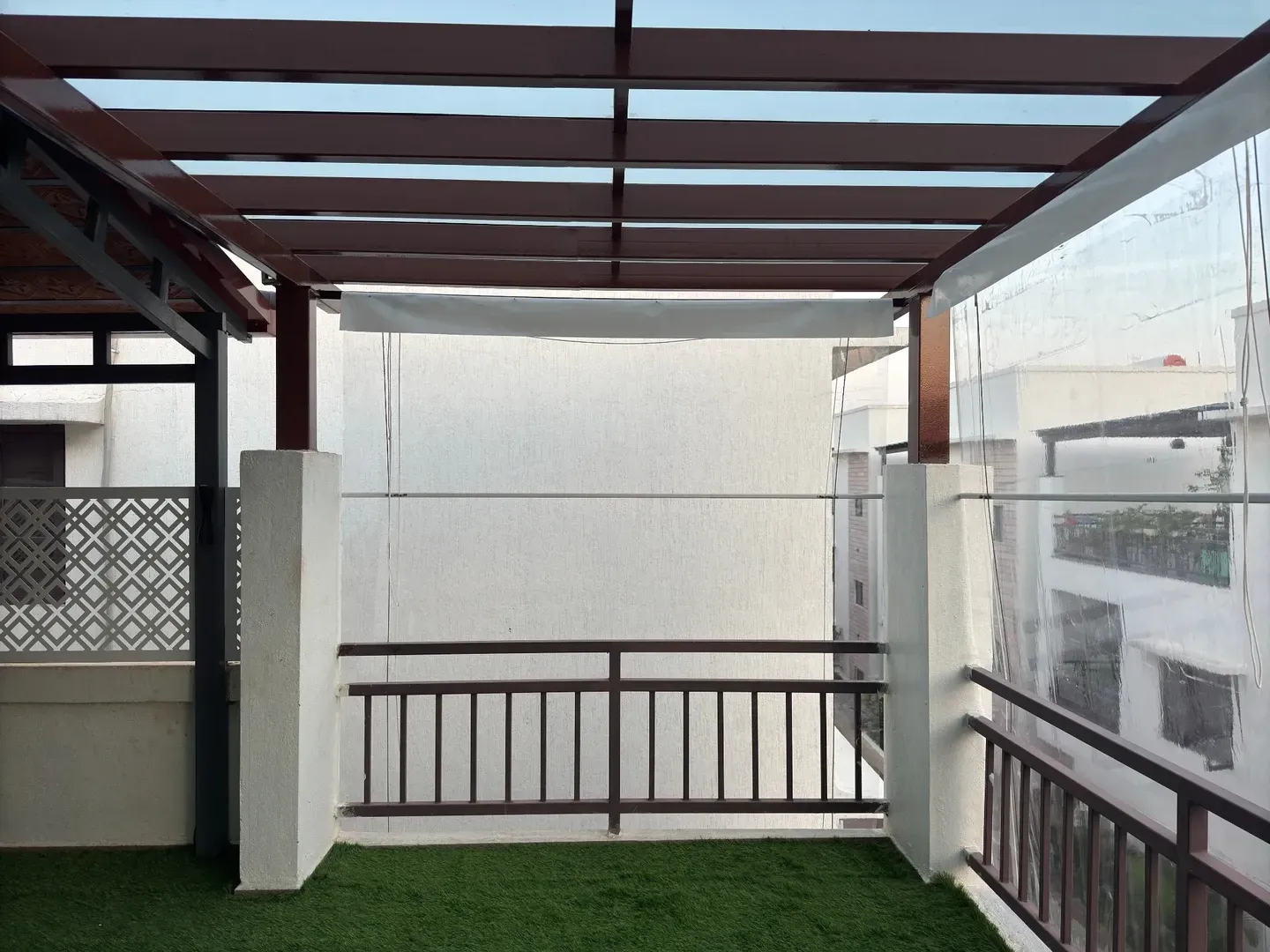 Glass roof and dark rafters over a terrace corner with green flooring and metal railing