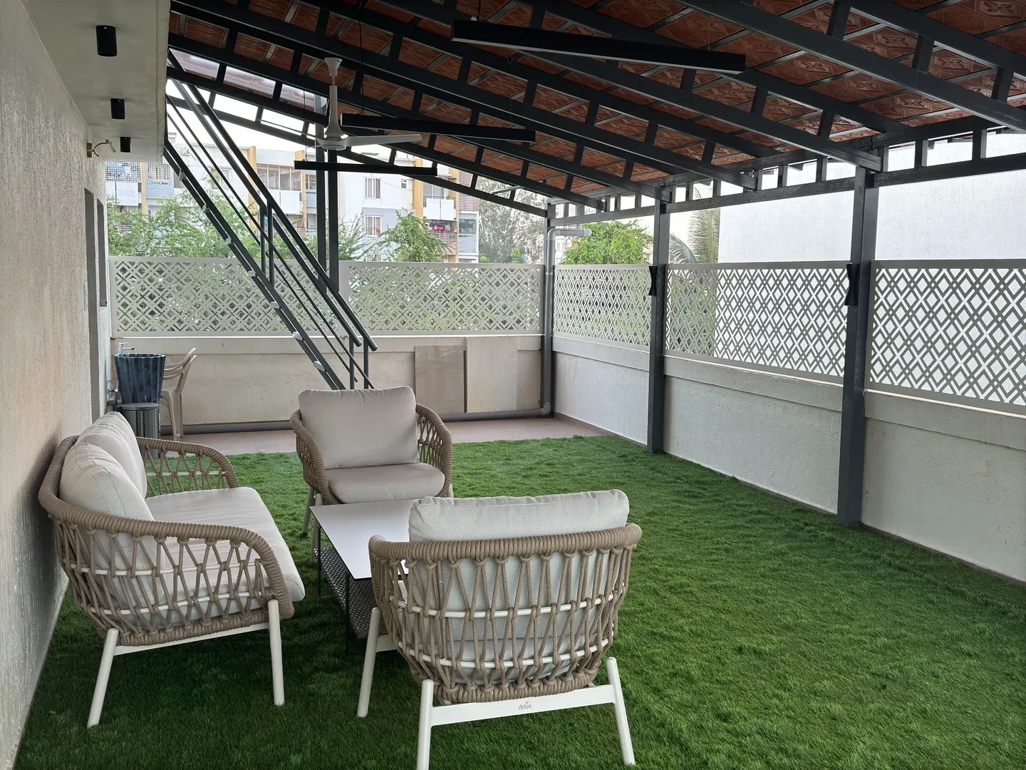 Outdoor seating beneath the tile roof beside the staircase and white patterned screens
