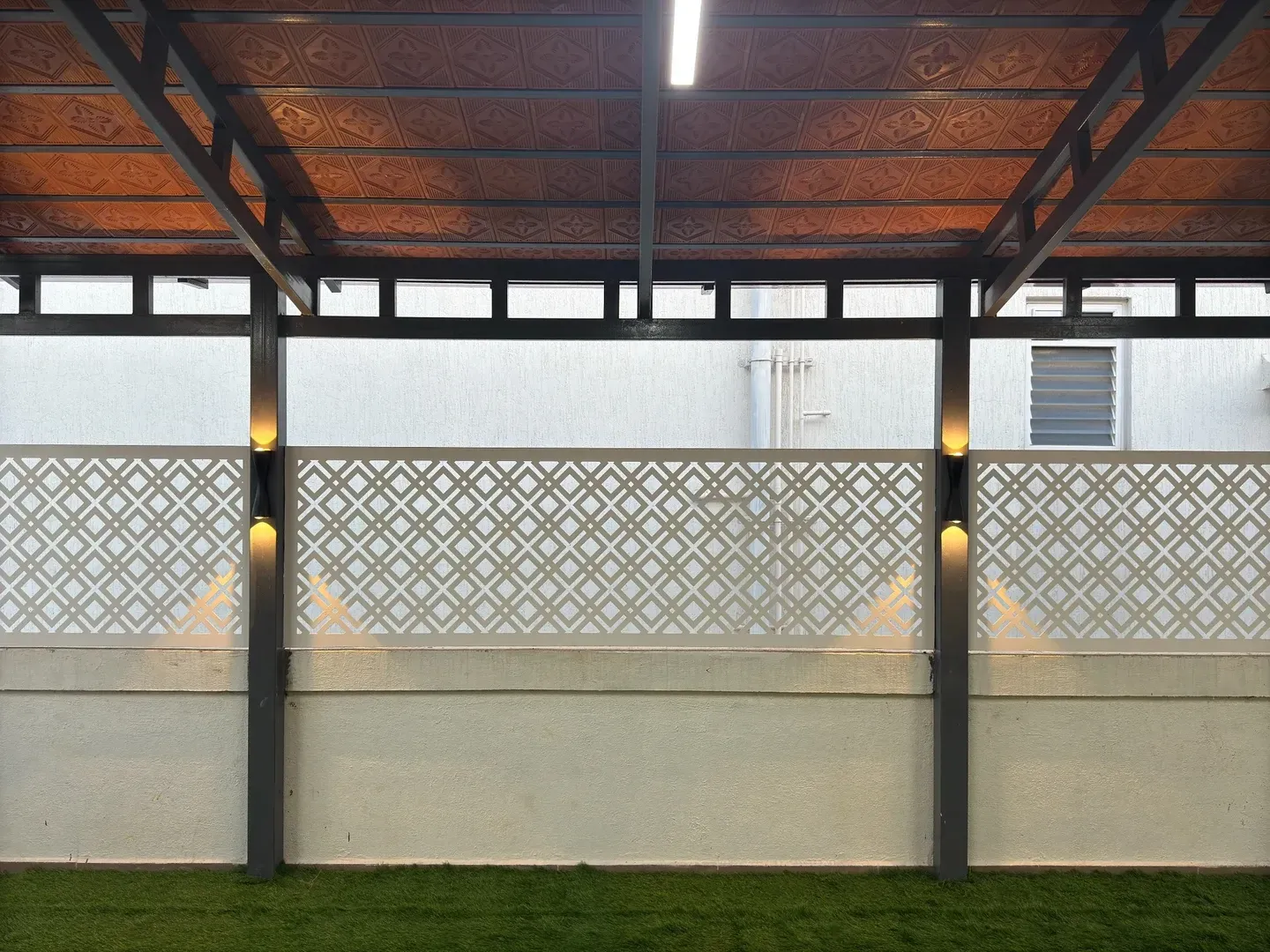 White CNC boundary panels with illuminated dark posts and a light beneath the tiled roof