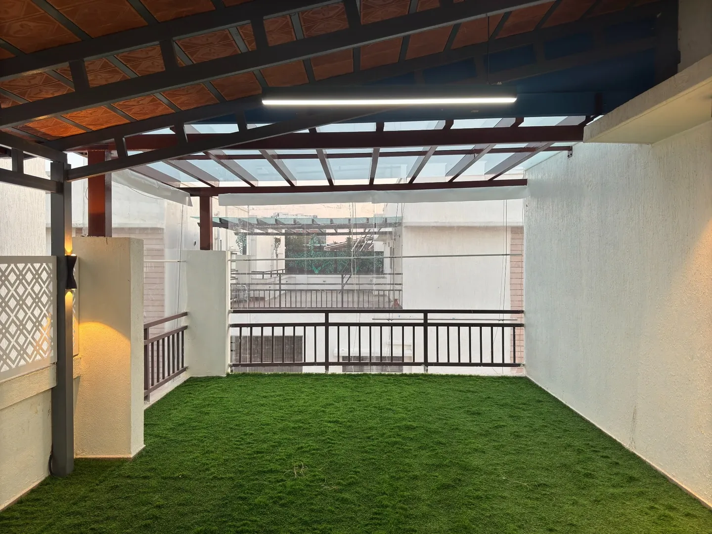 View towards the glass pergola with illuminated posts, green flooring and metal railing