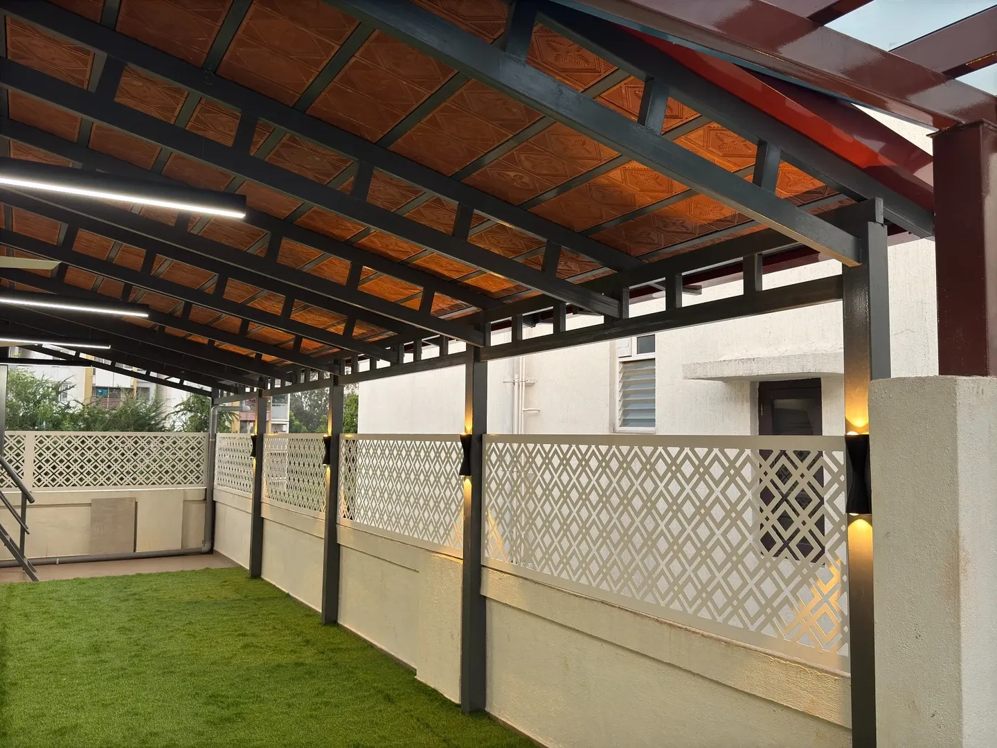 Tiled pergola roof with dark rafters above white patterned fencing and warm post lights