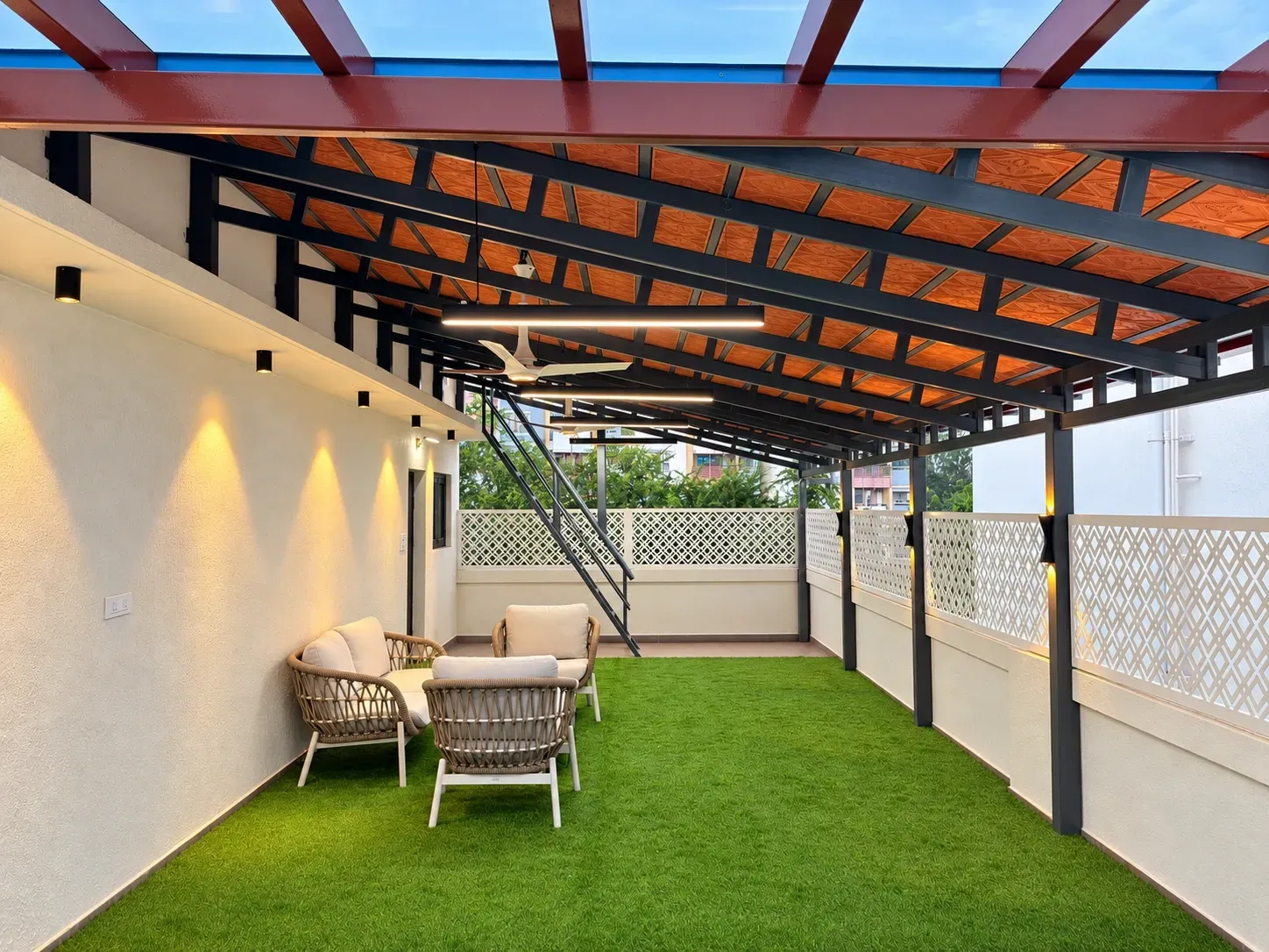 Enhanced view of Jancy’s illuminated terrace with Mangalore tile and glass roofing, dark rafters, white CNC fencing, a staircase and green flooring