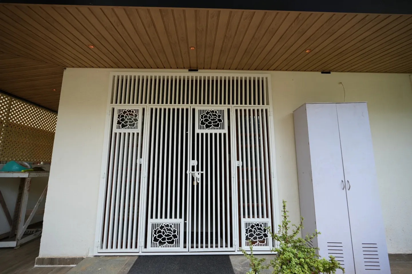 White metal entrance gate with decorative panels beneath a timber-toned ceiling