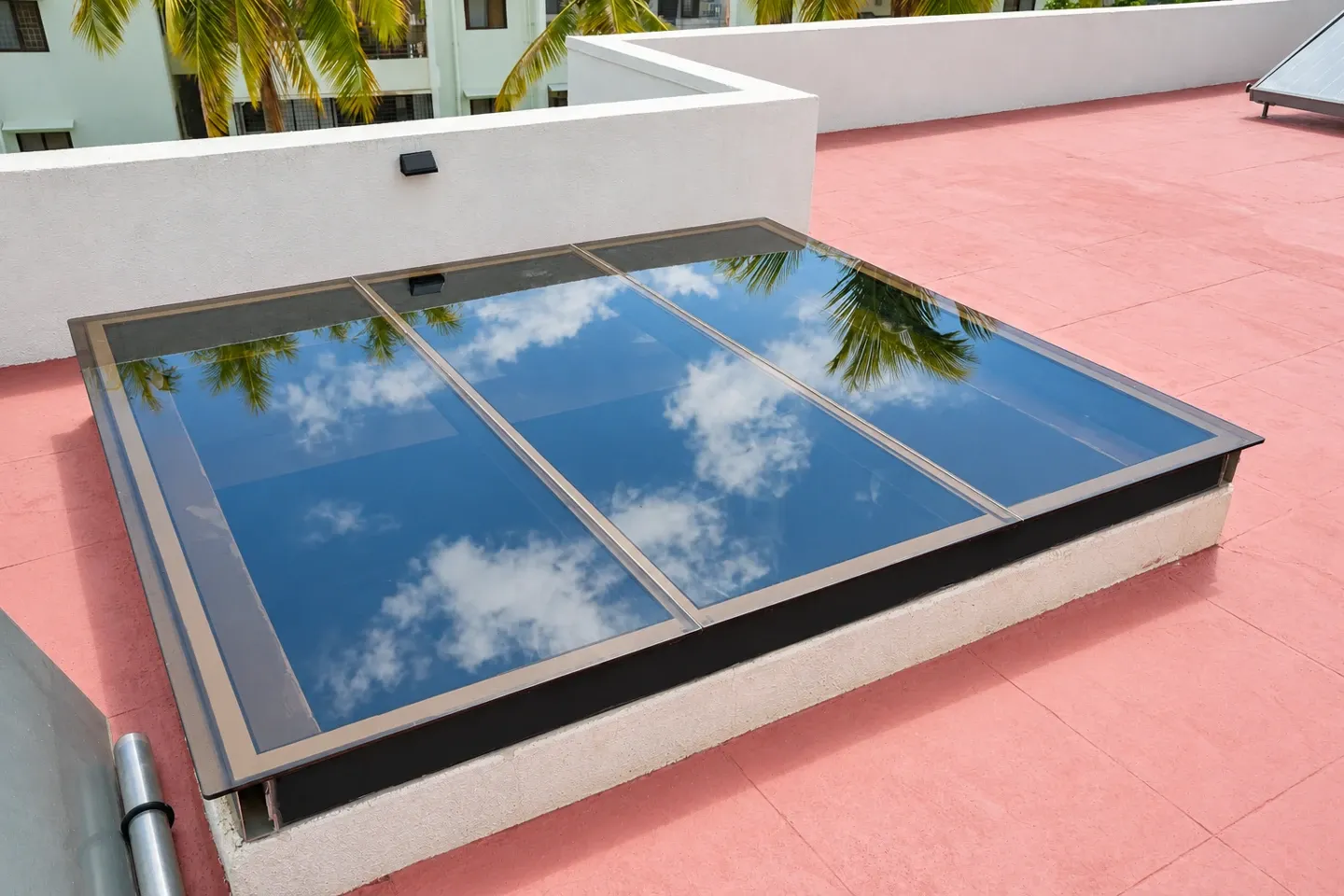 Enhanced view of a framed glass skylight reflecting the sky on a red terrace floor