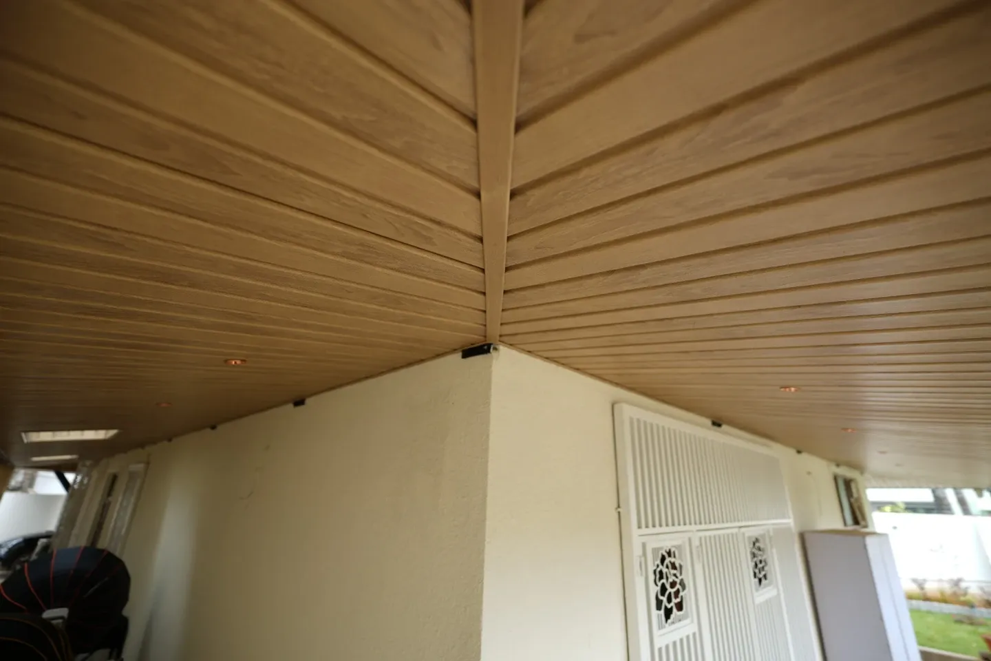 Upward view of timber-toned ceiling panels meeting at the corner above the white entrance gate
