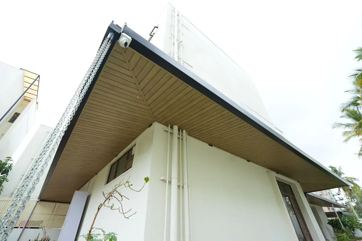 Upward exterior view of the canopy roof edge, timber-toned underside and rain chain