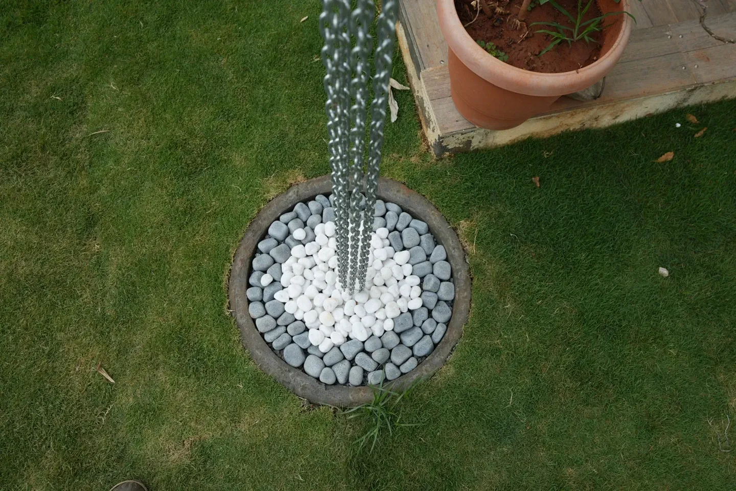 Close view of a metal rain chain ending in a circular arrangement of white and dark pebbles