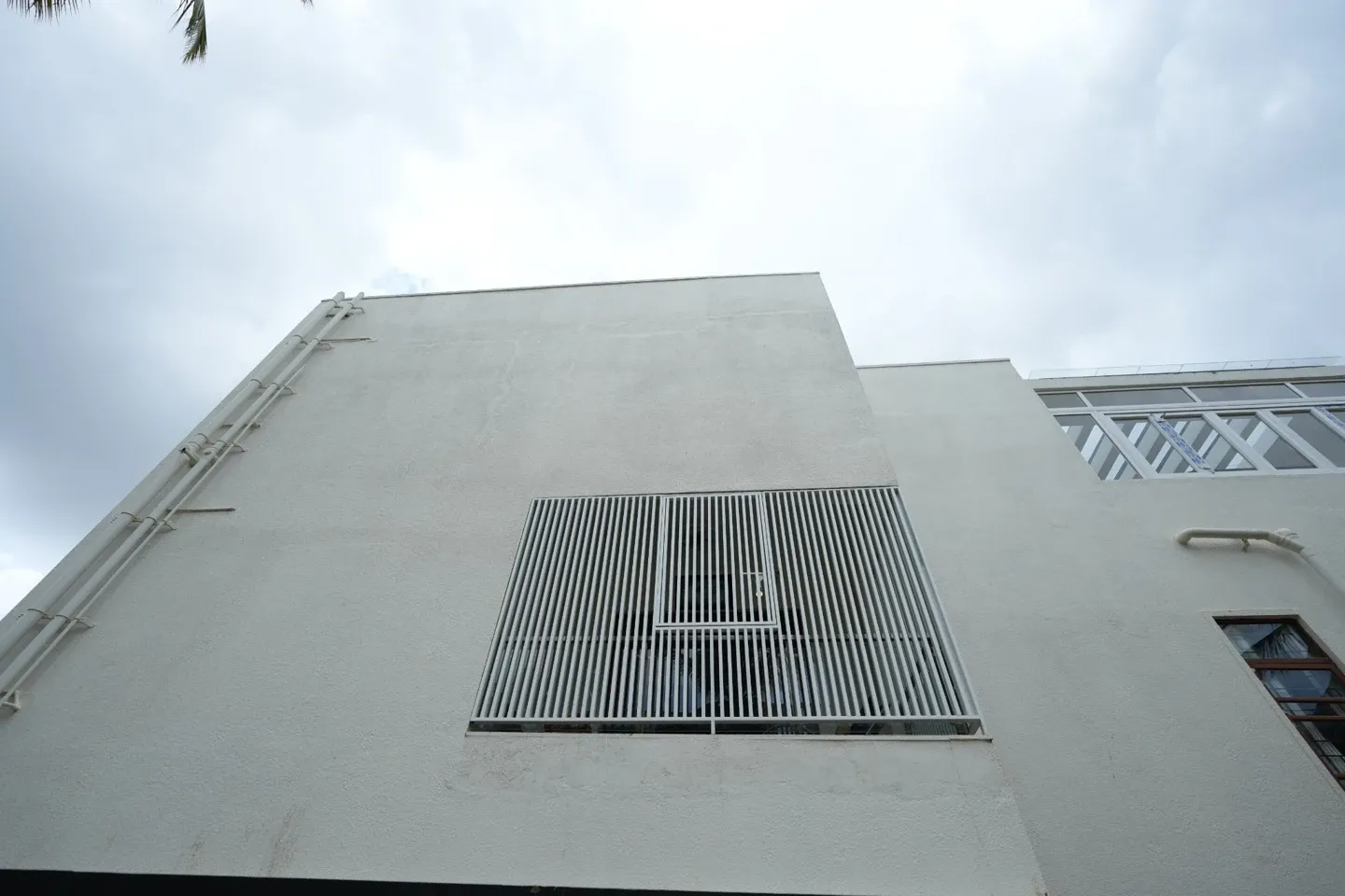 Upward view of a white building wall with a tall vertical-bar window screen