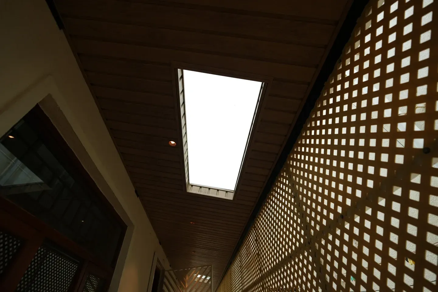 Upward view of a rectangular skylight in a timber-toned canopy beside lattice screening