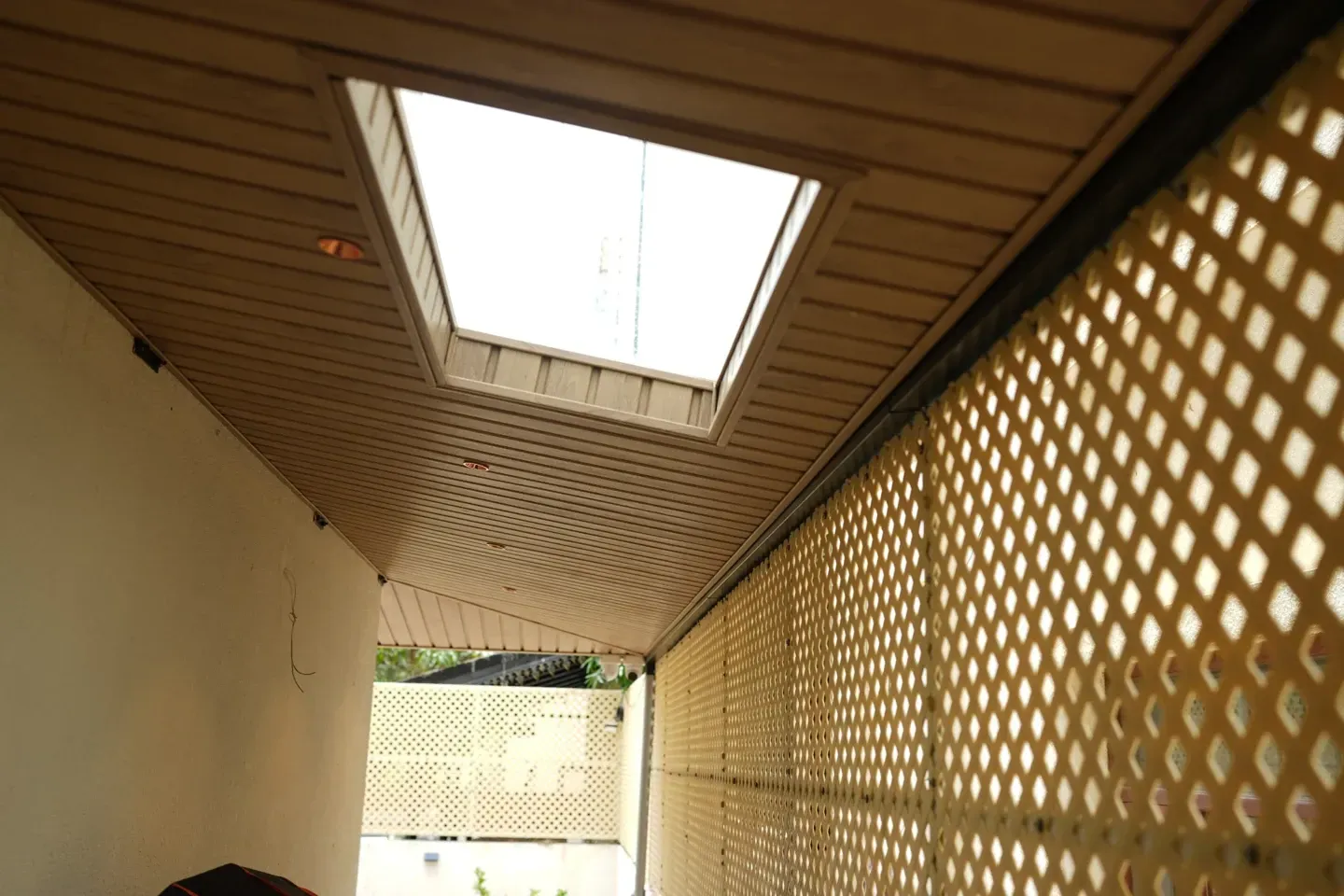 View along a timber-toned canopy ceiling with a rectangular skylight and lattice side panels