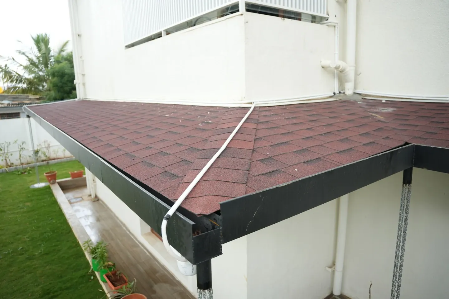 View of red asphalt shingles and dark edge flashing on the villa canopy