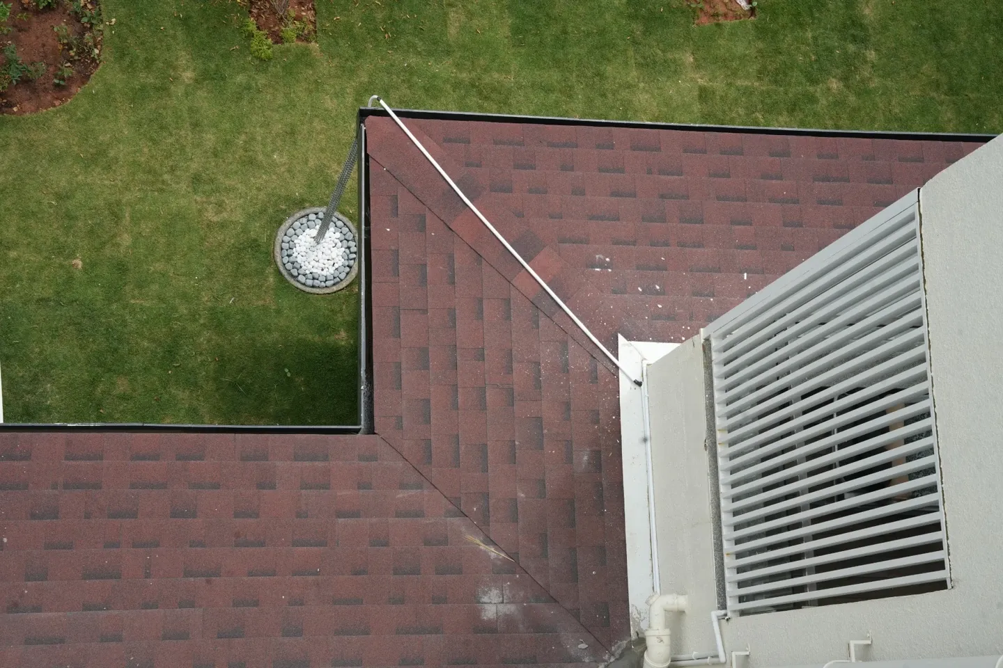 Top view of a red shingles roof corner beside a garden and window screen