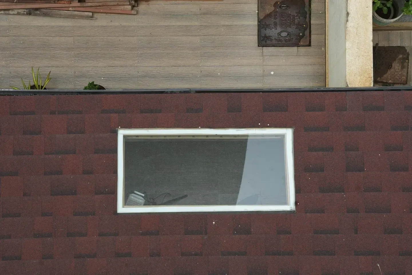 Close overhead view of a white-framed rectangular skylight surrounded by red shingles