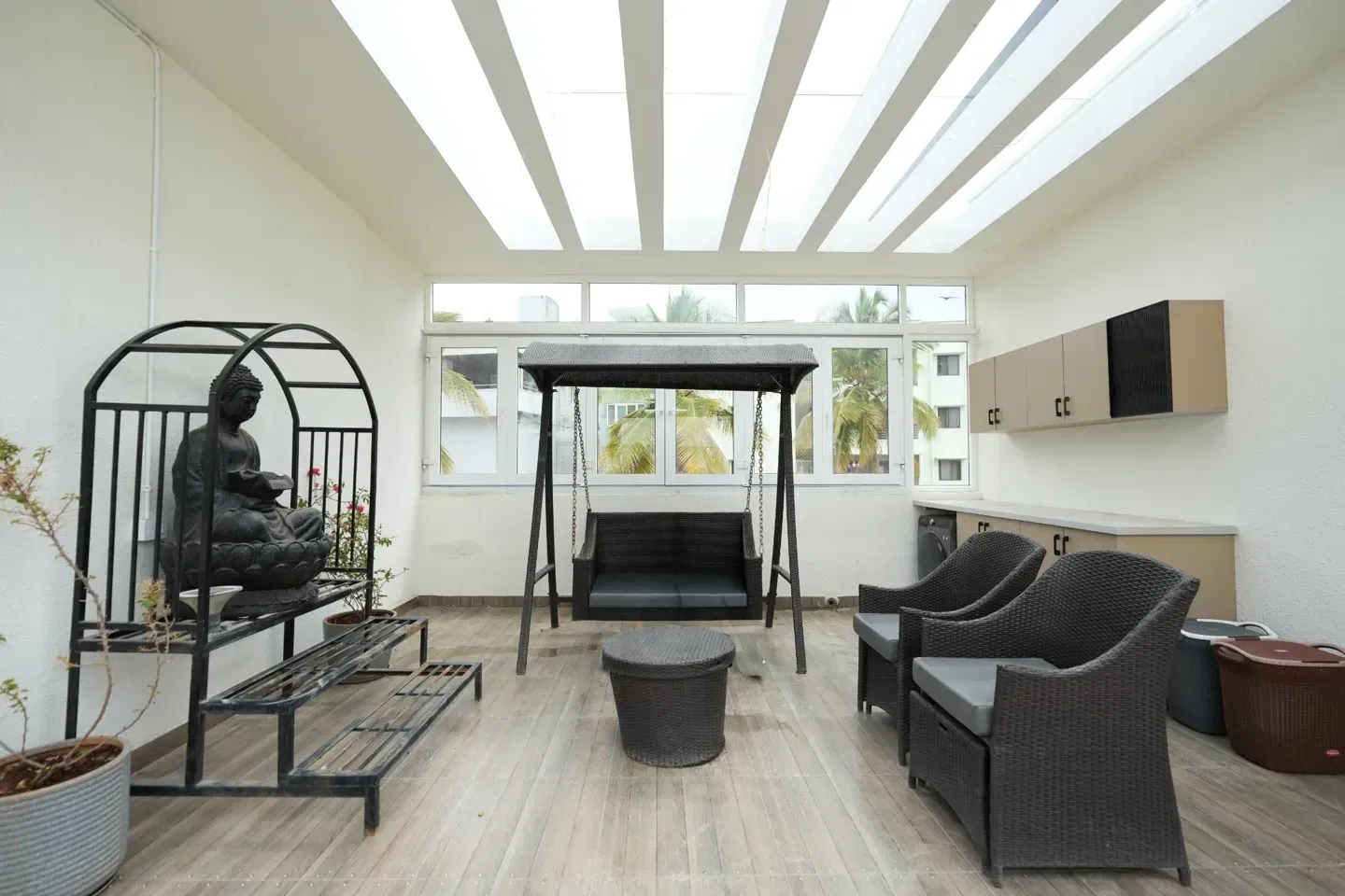 Bright glazed-roof seating space with white rafters, a swing, chairs and a sculpture