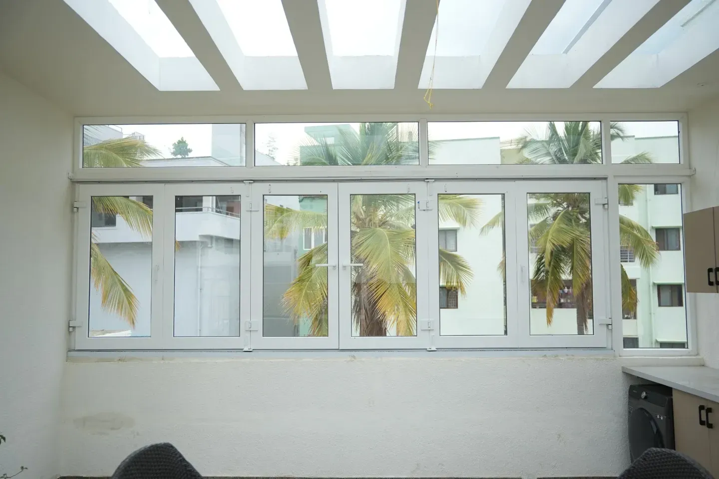 White-framed windows beneath a glazed roof with white rafters inside Jayashree’s home