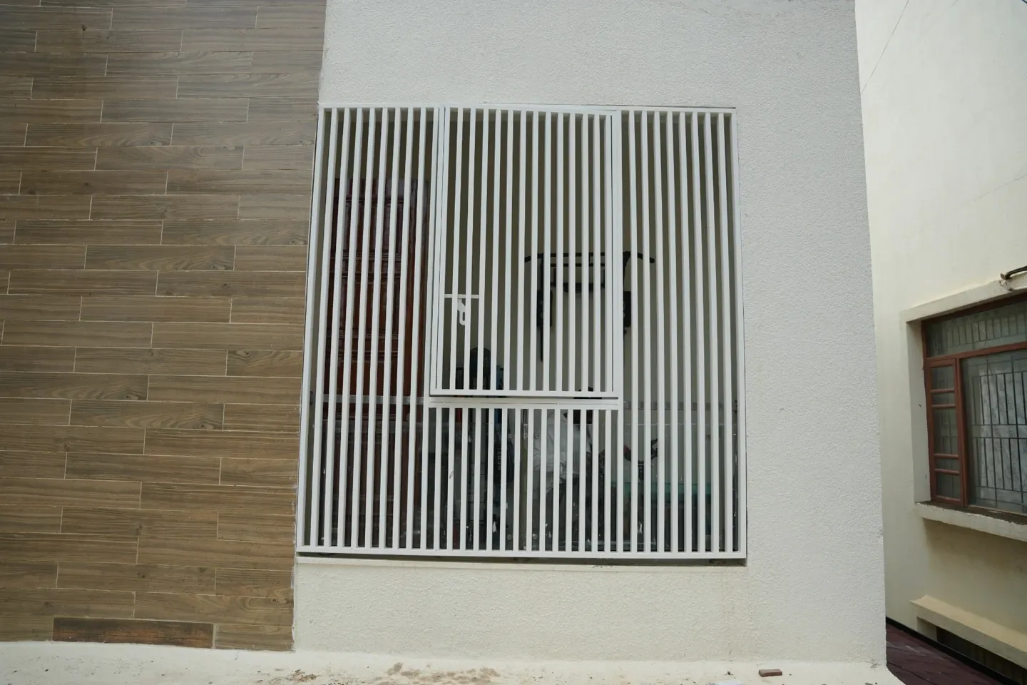 White vertical-bar metal screen around a window beside a textured facade wall