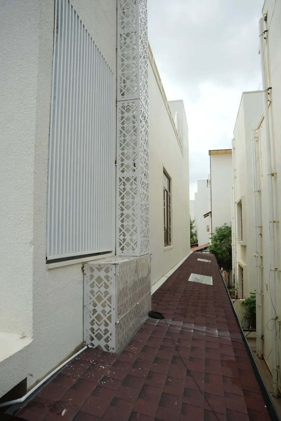 Portrait view along the red shingles canopy with white window screens and patterned metalwork