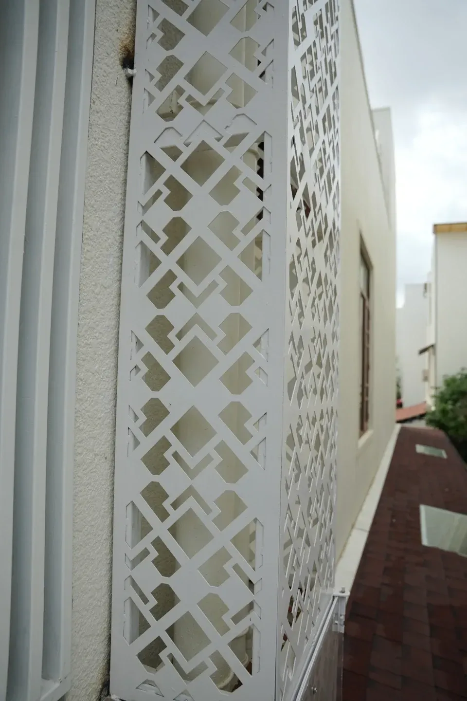 Close portrait view of a white geometric metal panel beside window screening above the shingles roof