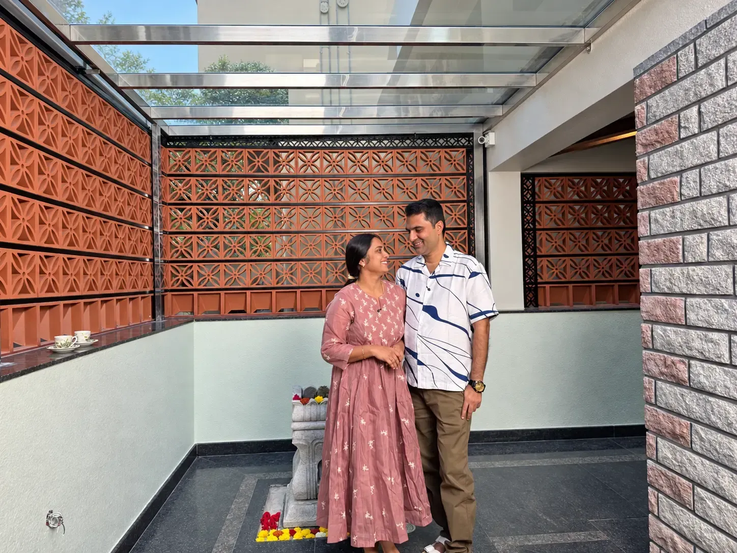 Couple standing beside terracotta jali privacy walls beneath a glass pergola