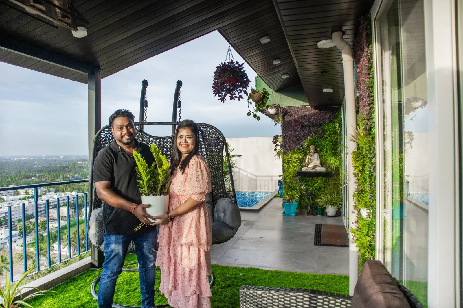 Couple holding a potted plant on their covered terrace beside a hanging chair