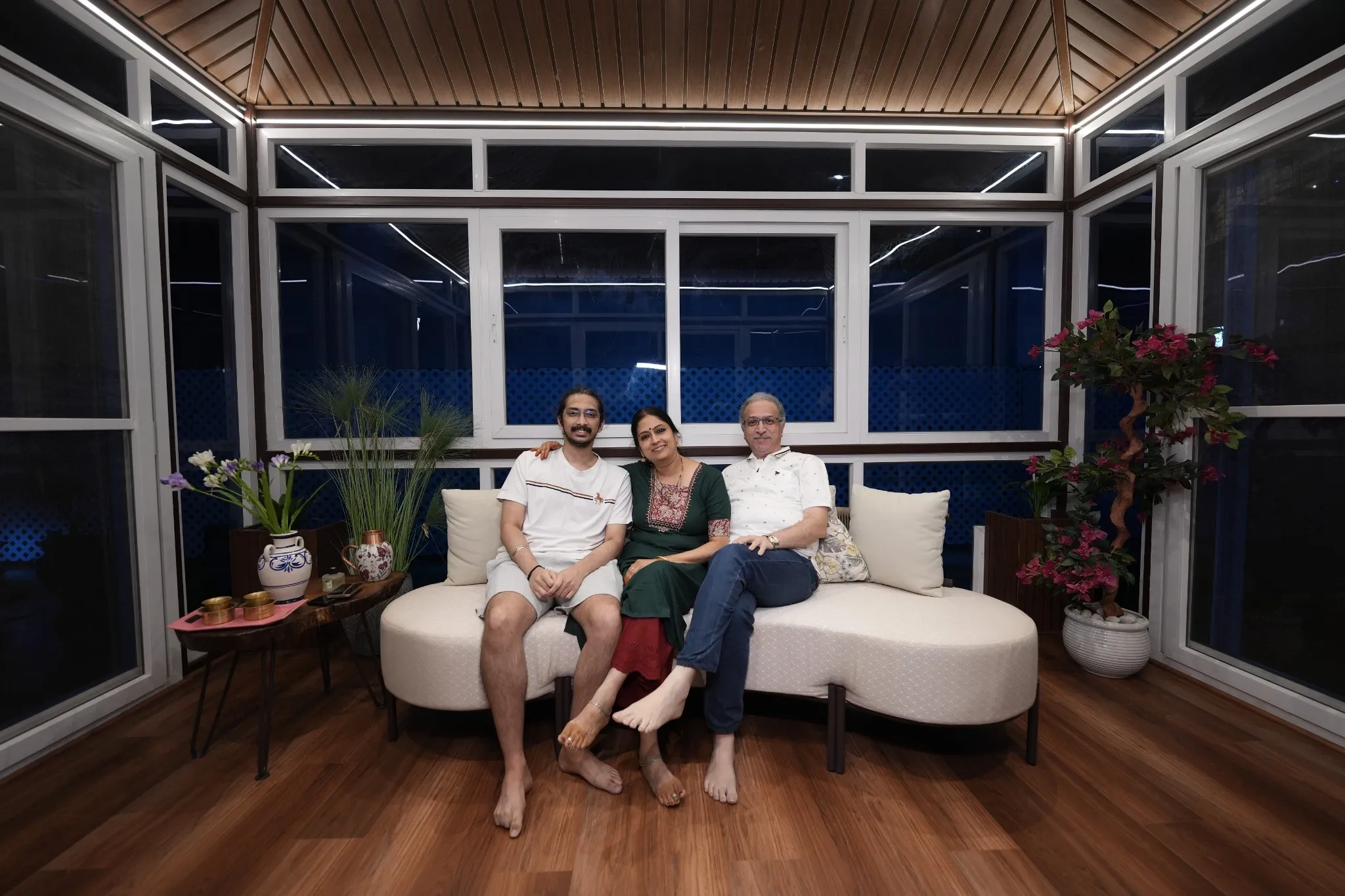 Three people seated in a glass-enclosed terrace lounge at night