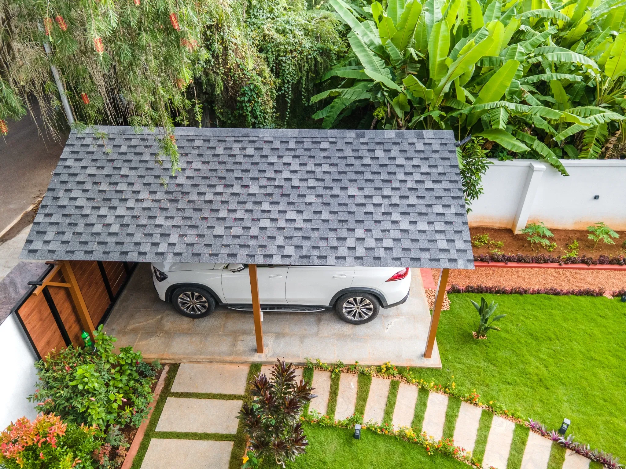 Aerial view of a shingle-roof car parking pergola beside a landscaped garden