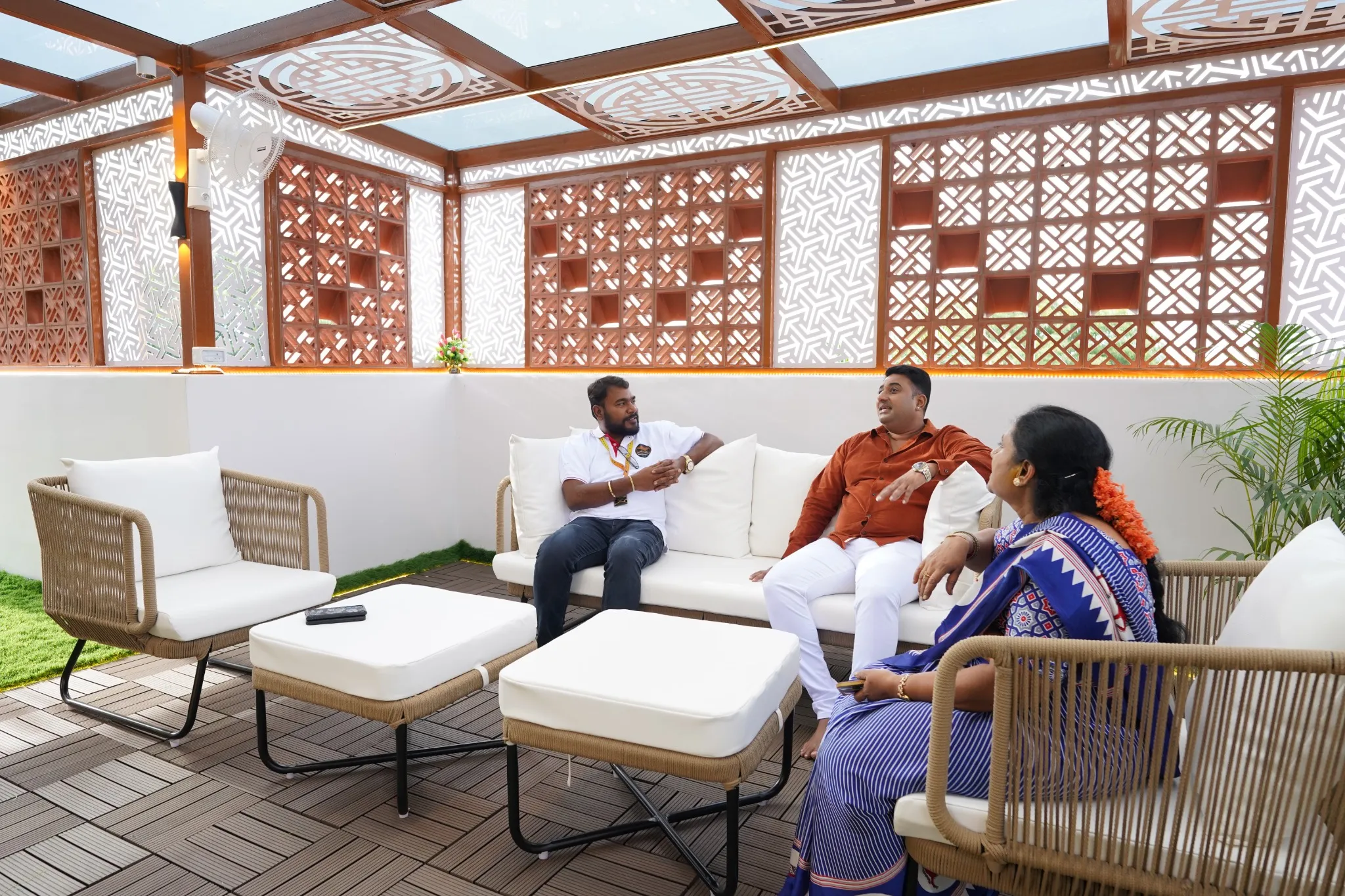 Customers and a Pergola Design.in team member seated inside a completed premium pergola with decorative privacy panels and glass roofing